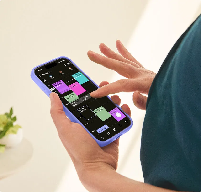 A woman’s hands holding a phone displaying a color-coded calendar