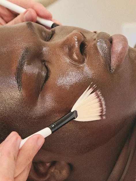 A woman getting her face brushed with two fan brushes