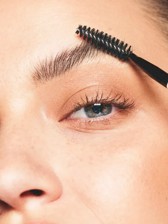 A spoolie combing through a woman’s eyebrow
