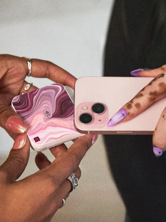 A woman’s manicured hand holding her phone over a patterned GlossGenius Tap & Go reader held by another pair of manicured hands