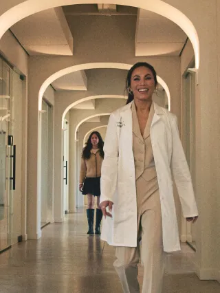 A medspa professional in a white coat leading her client down a hallway