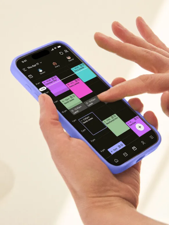 A woman’s hands holding a phone displaying a color-coded calendar