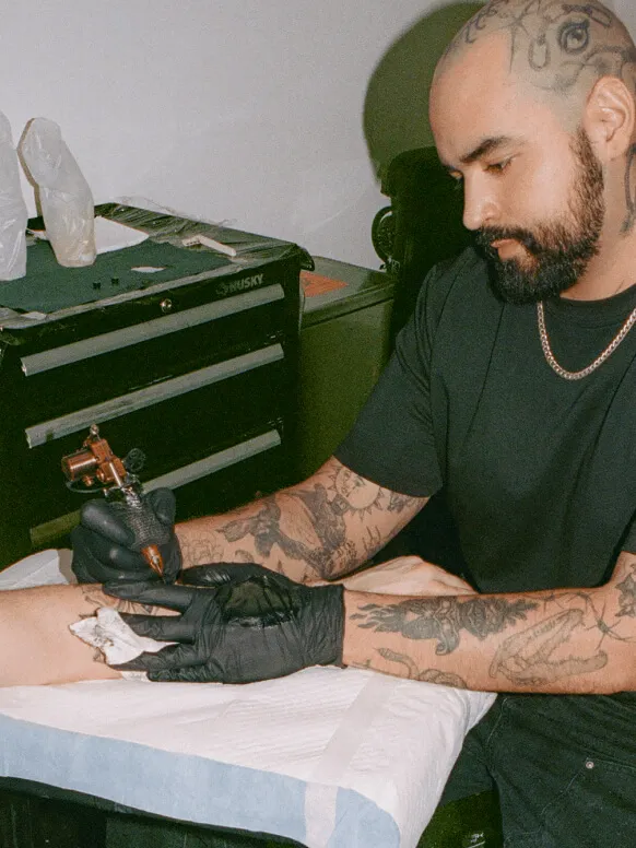 Man with tattooed arms and head tattooing his client’s arm