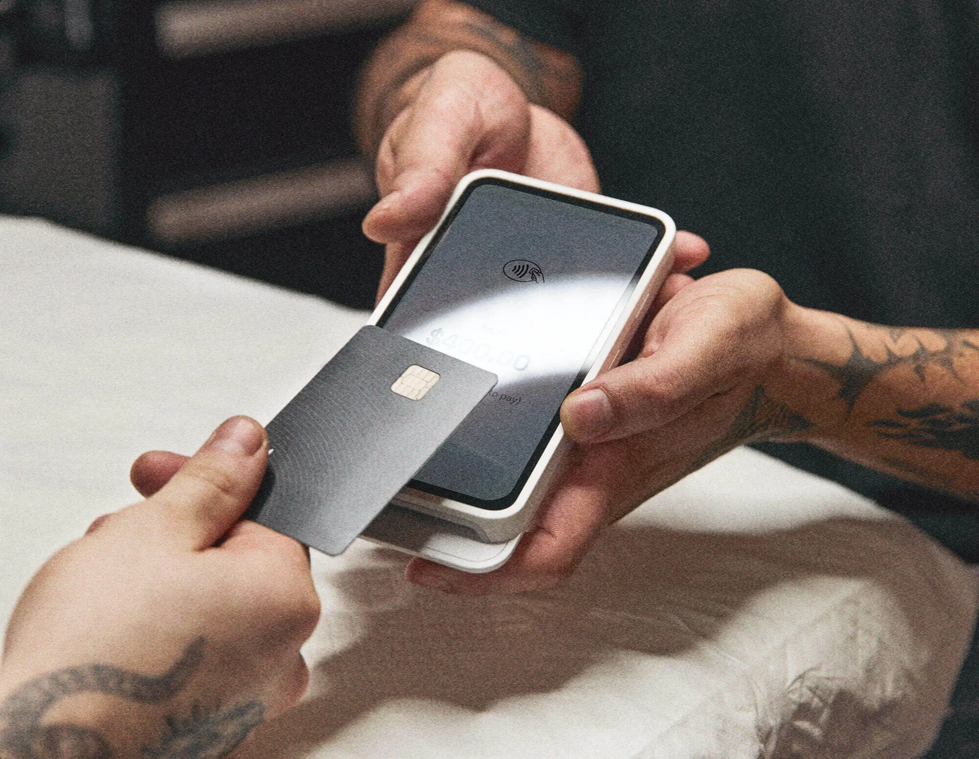 A hand holding a black credit card over a mobile phone held by two other hands
