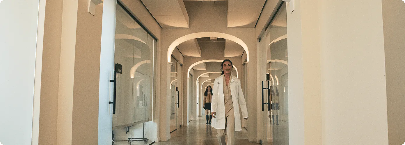 A medspa professional in a white coat leading her client down a hallway