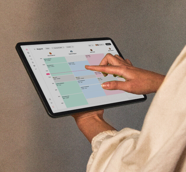 Someone’s hands holding a tablet displaying the GlossGenius Sola salon software calendar – an alternative to Vagaro Pro for Sola businesses.