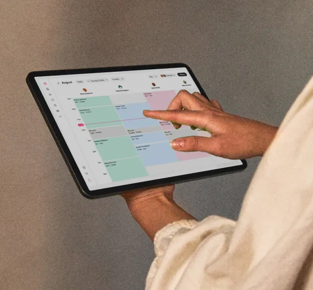 Someone’s hands holding a tablet displaying the GlossGenius Sola salon software calendar – an alternative to Vagaro Pro for Sola businesses.