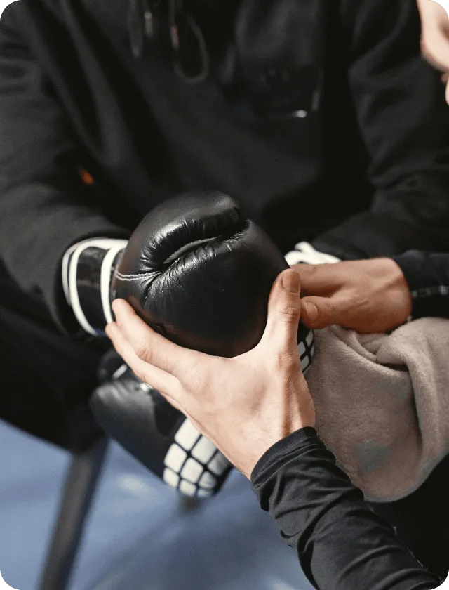 A hand holding another person’s hand with black boxing gloves on.