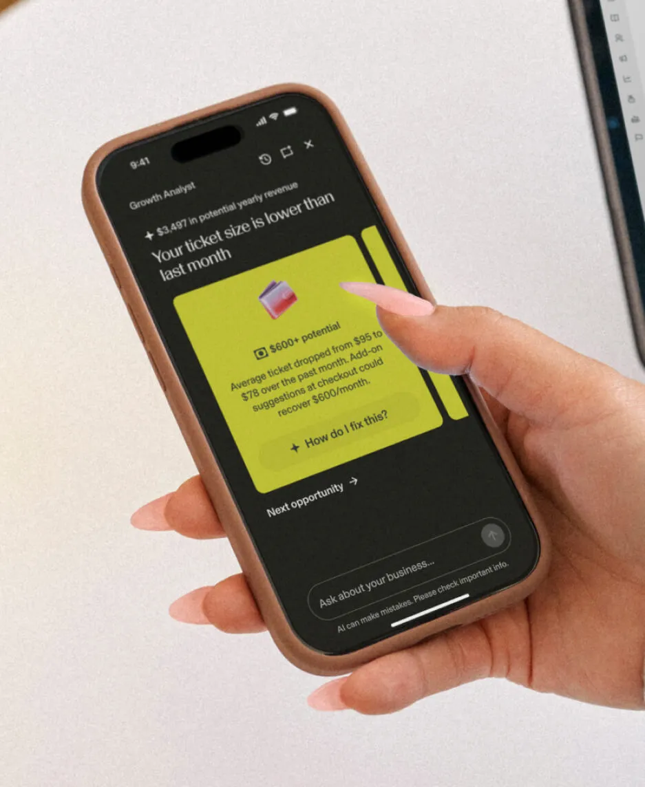 A phone held in a manicured hand displaying the GlossGenius Growth Analyst for a behavioral health practice.