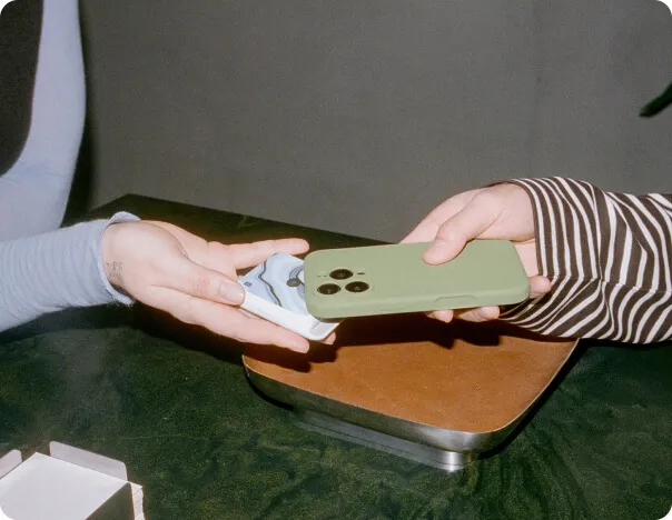Hands tapping a phone with a green silicone case to a GlossGenius Tap & Go POS system credit card reader to pay.