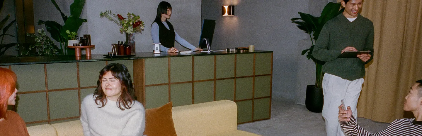 People sitting in a reception area of a beauty and wellness center, with a reception desk and receptionist behind it.