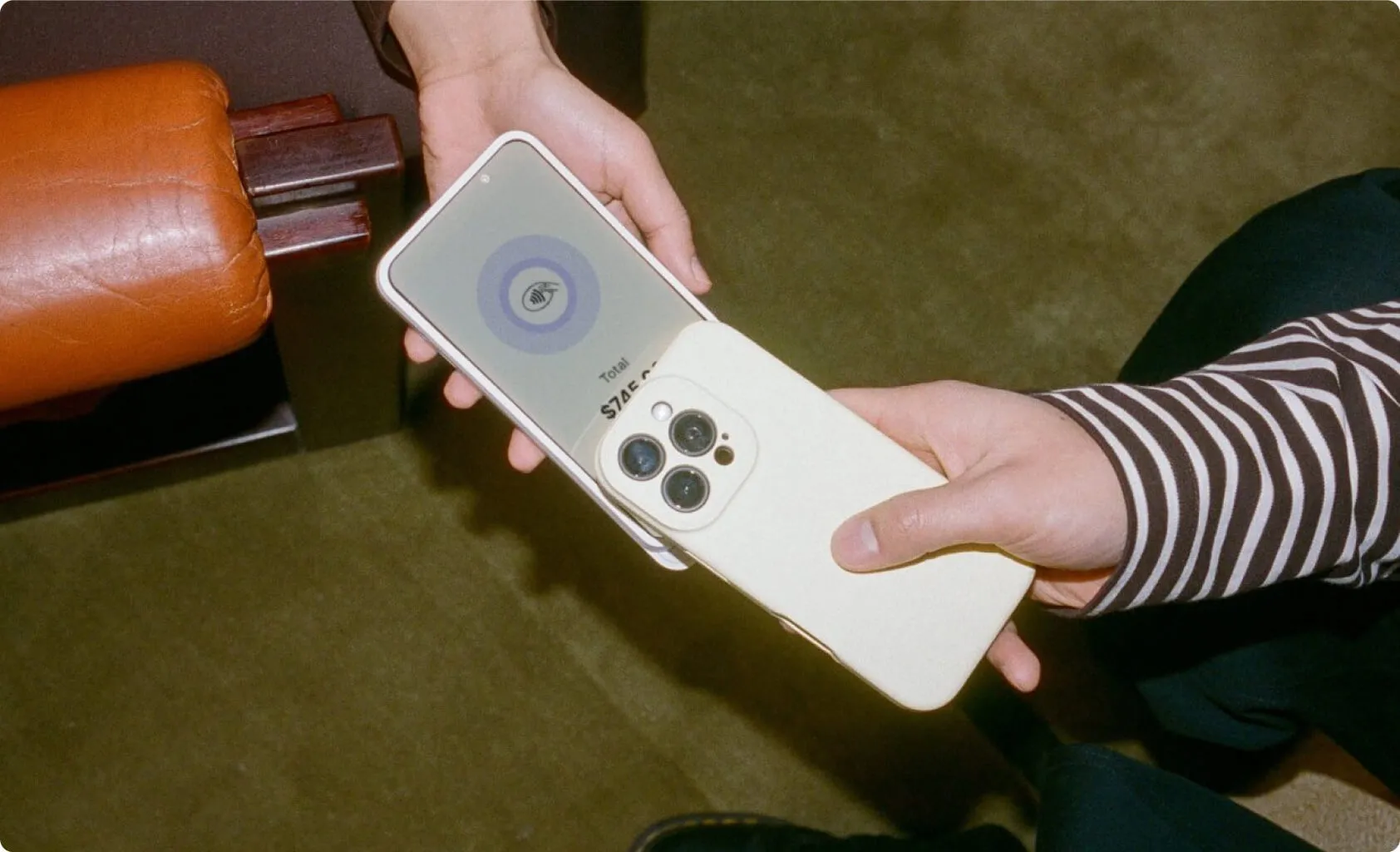 A hand holding a black credit card over a mobile phone held by two other hands