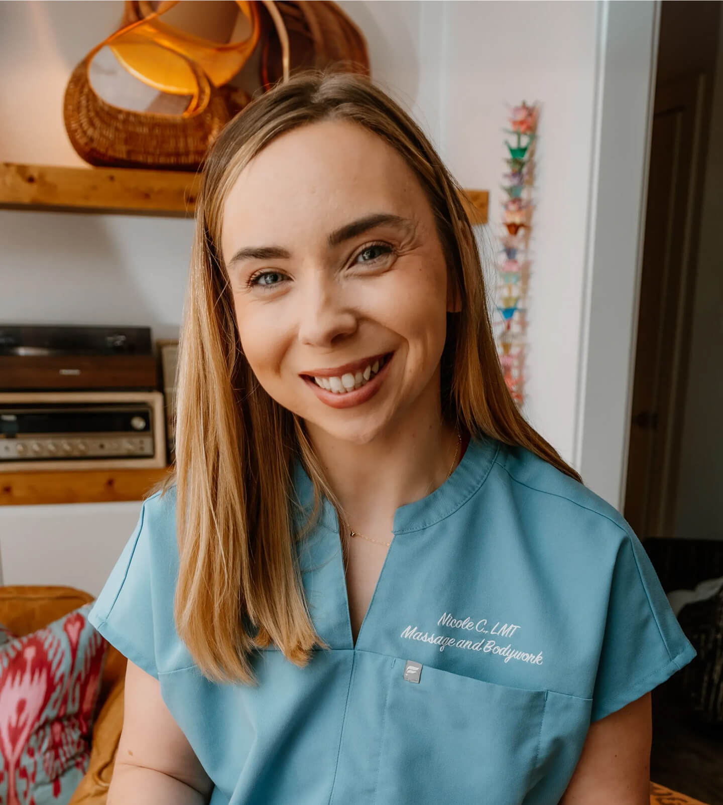 A headshot of Nicole Clayton from Nicole C., LMT Massage and Bodywork, who is smiling with pictures in the background.