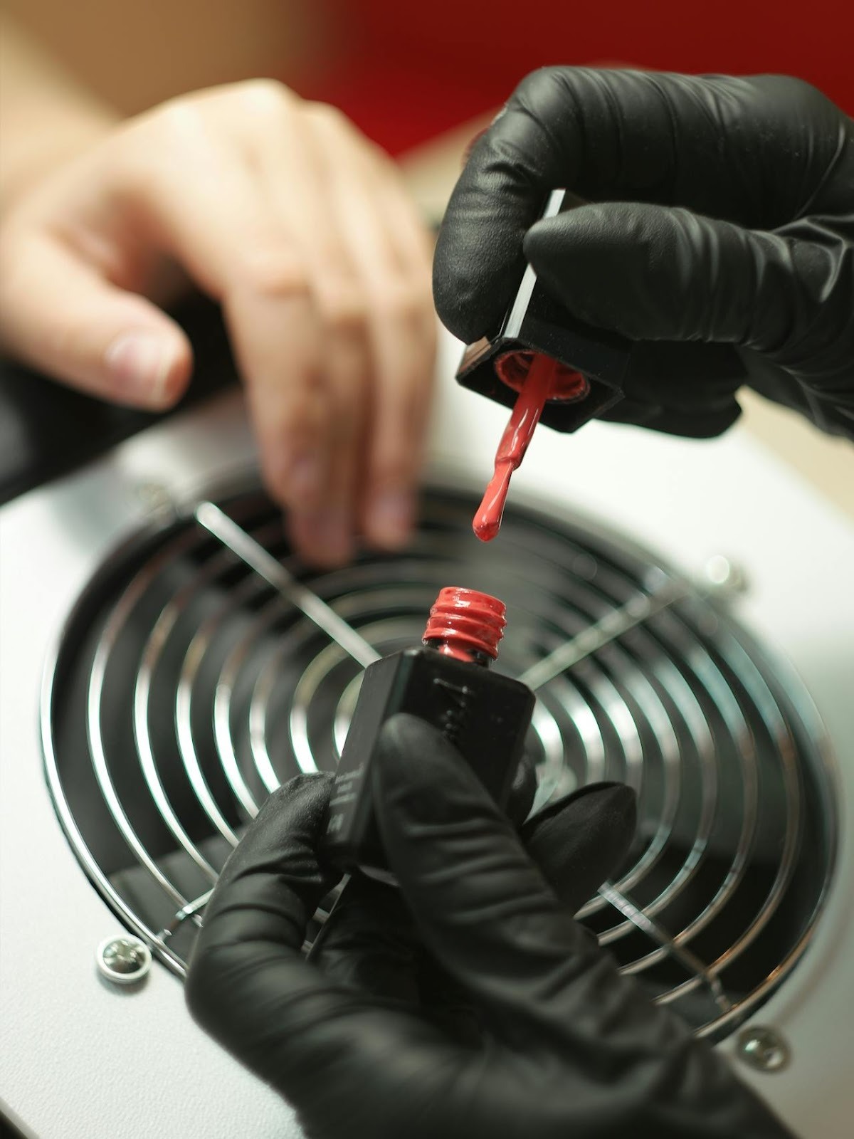 A nail tech applying red nail polish to a client's hand while using salon inventory software to track product usage