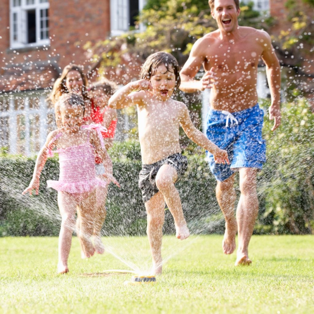 Parents and children running through sprinklers on a hot summer day