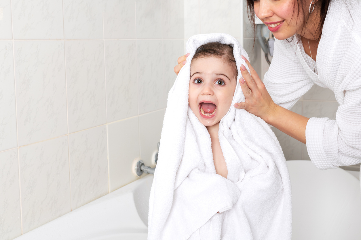 A child wrapped in a large white towel is dried off by their mom.