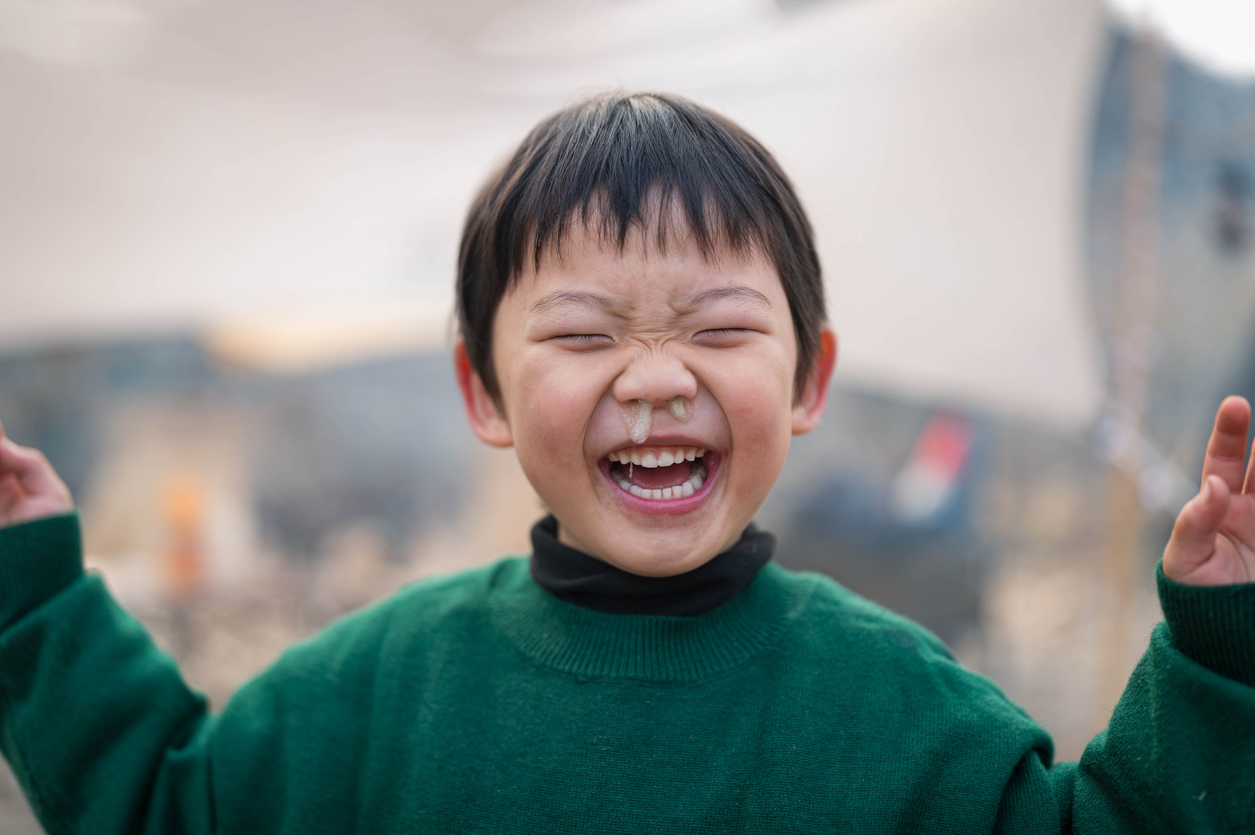 A little boy smiling with mucus coming out of his nose.