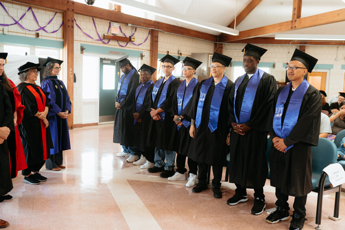a group of graduates stands with arms folded in a sunlit room