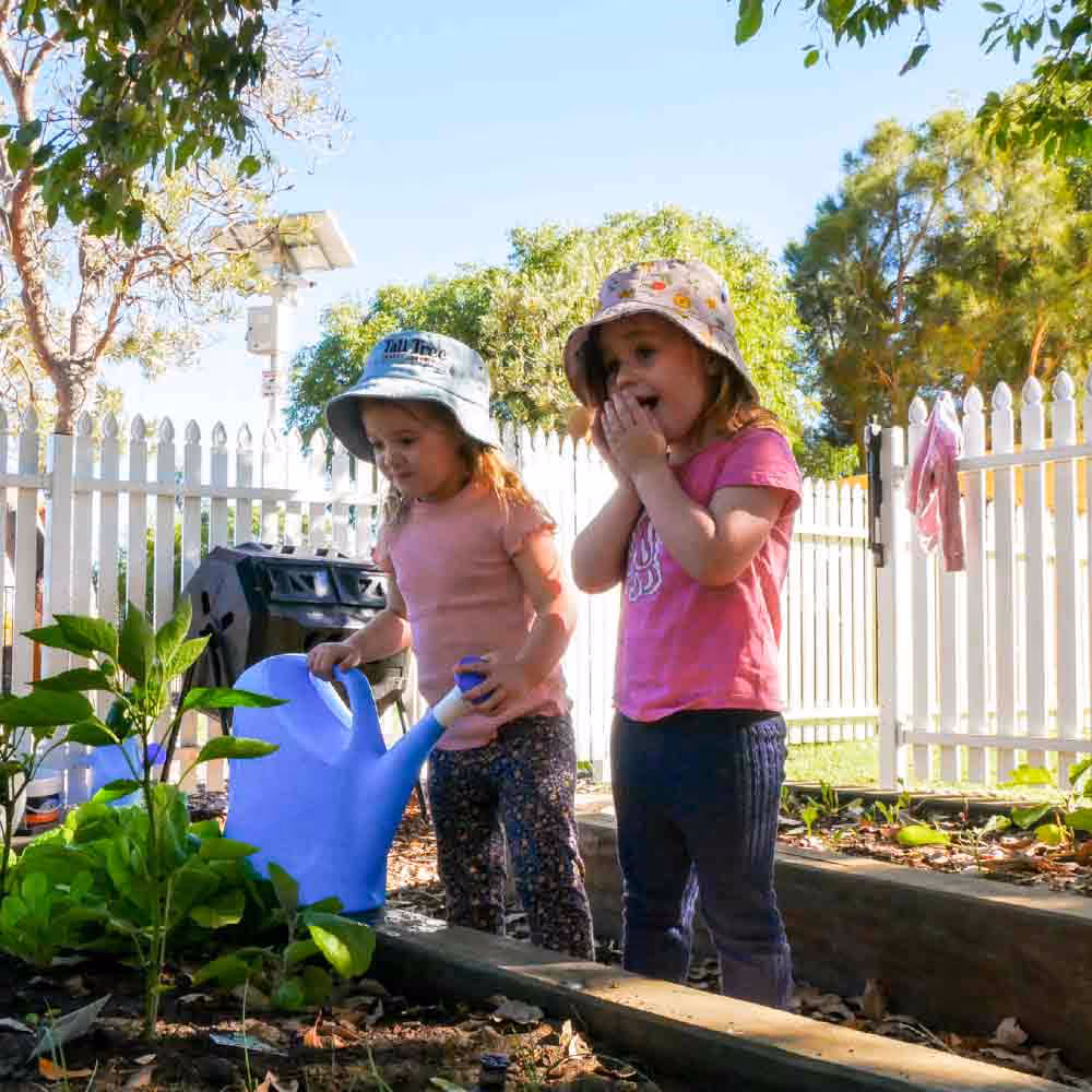 Two girls in garden playing with watering can