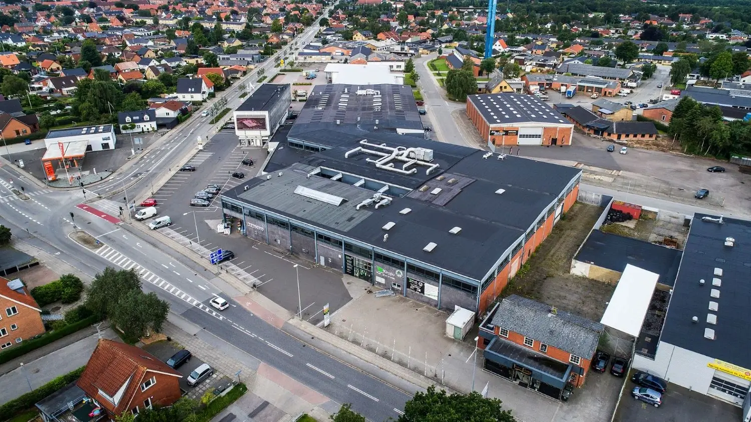Aerial view of a commercial building complex with large flat roofs and surrounding parking lots in a suburban area with residential houses and roads.
