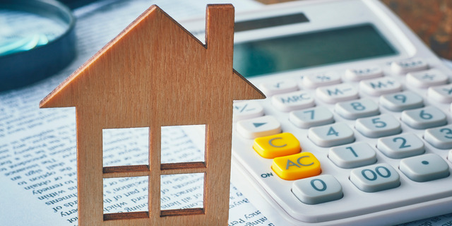 Wooden house model next to a calculator on financial documents, representing HOA dues, housing costs, and property expense planning in Southern California.