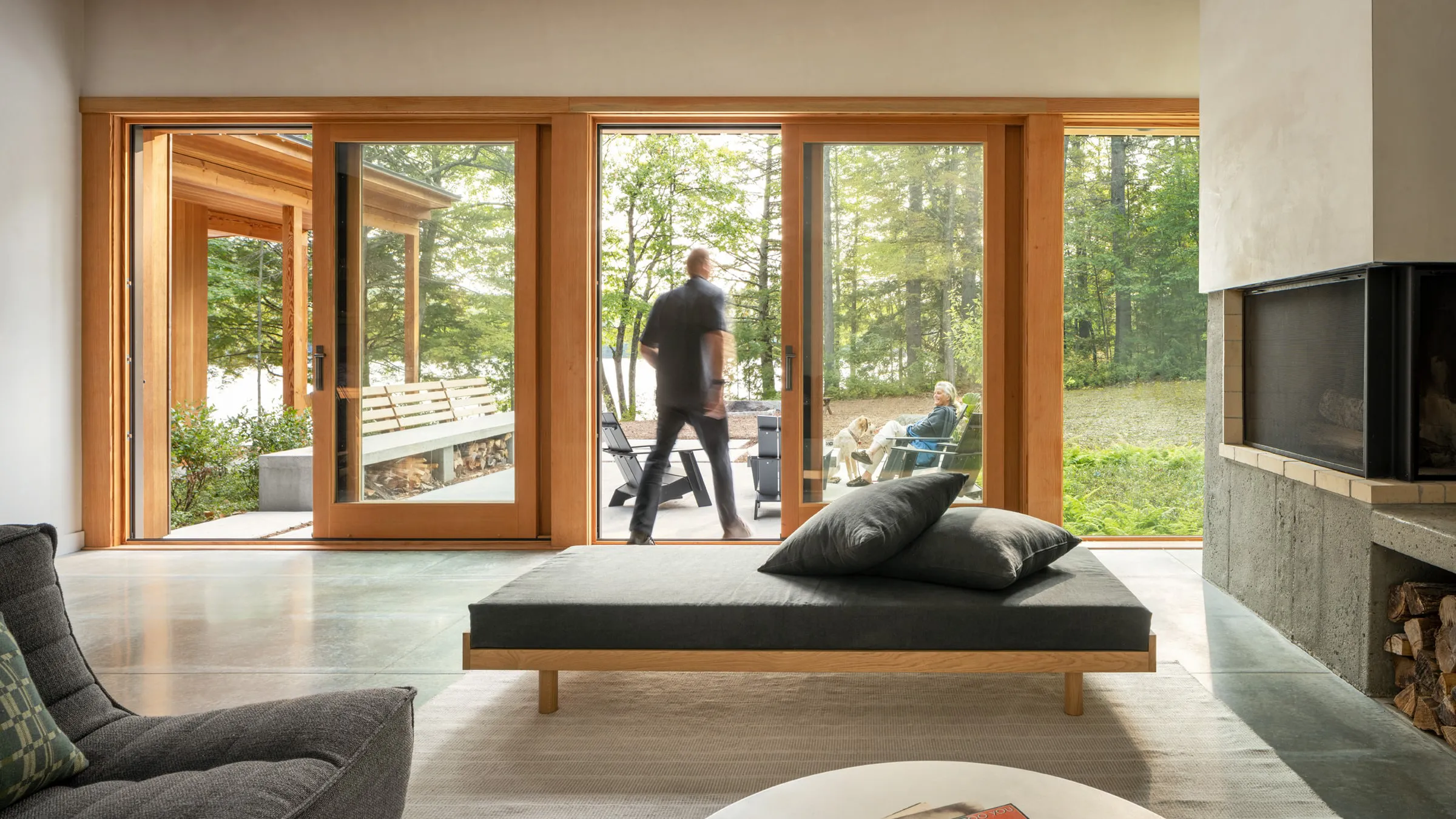 Modern living room with large wooden sliding glass doors opening to patio with people and a dog.