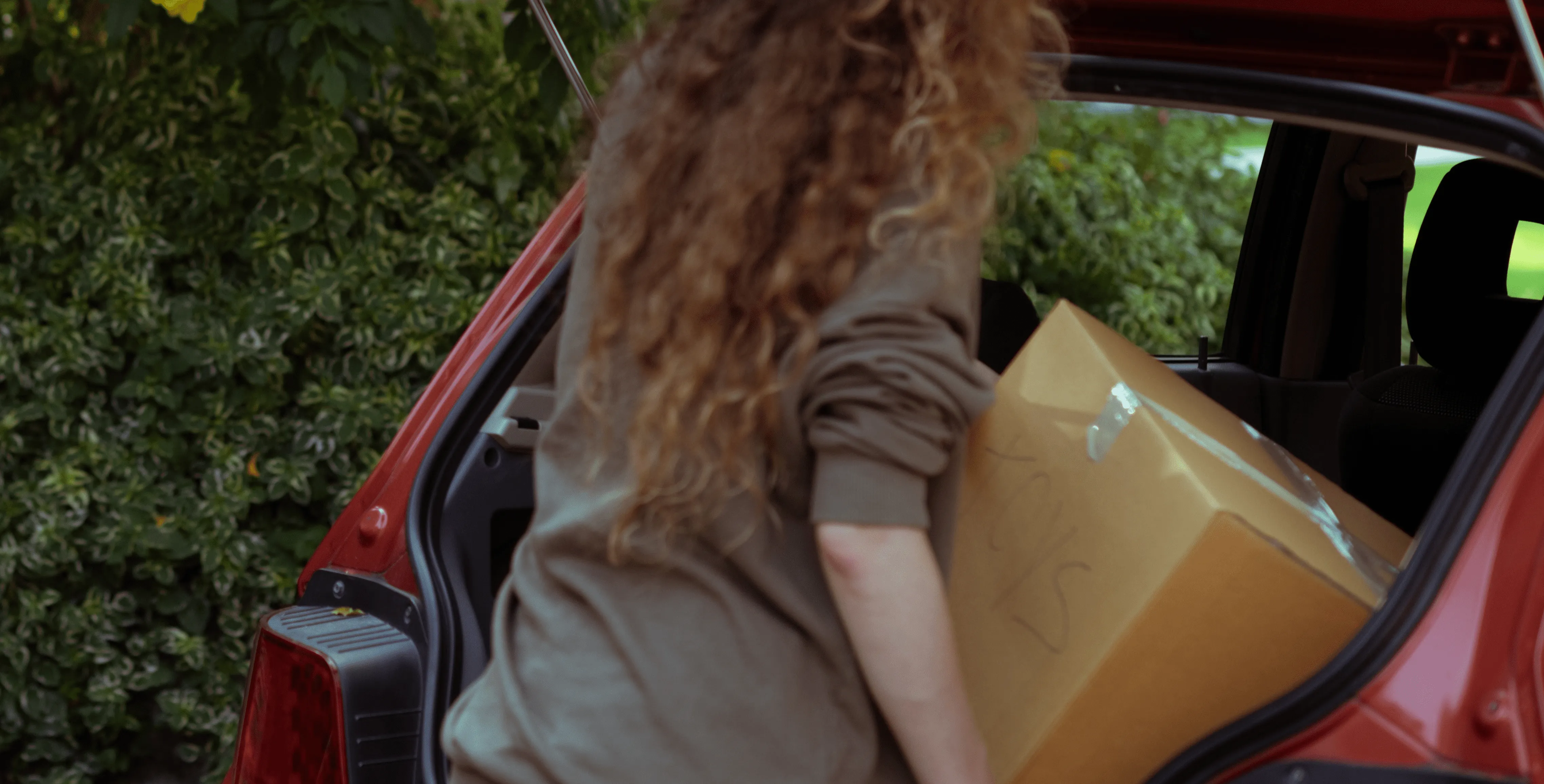chica con el pelo rizado metiendo una caja en el maletero del coche