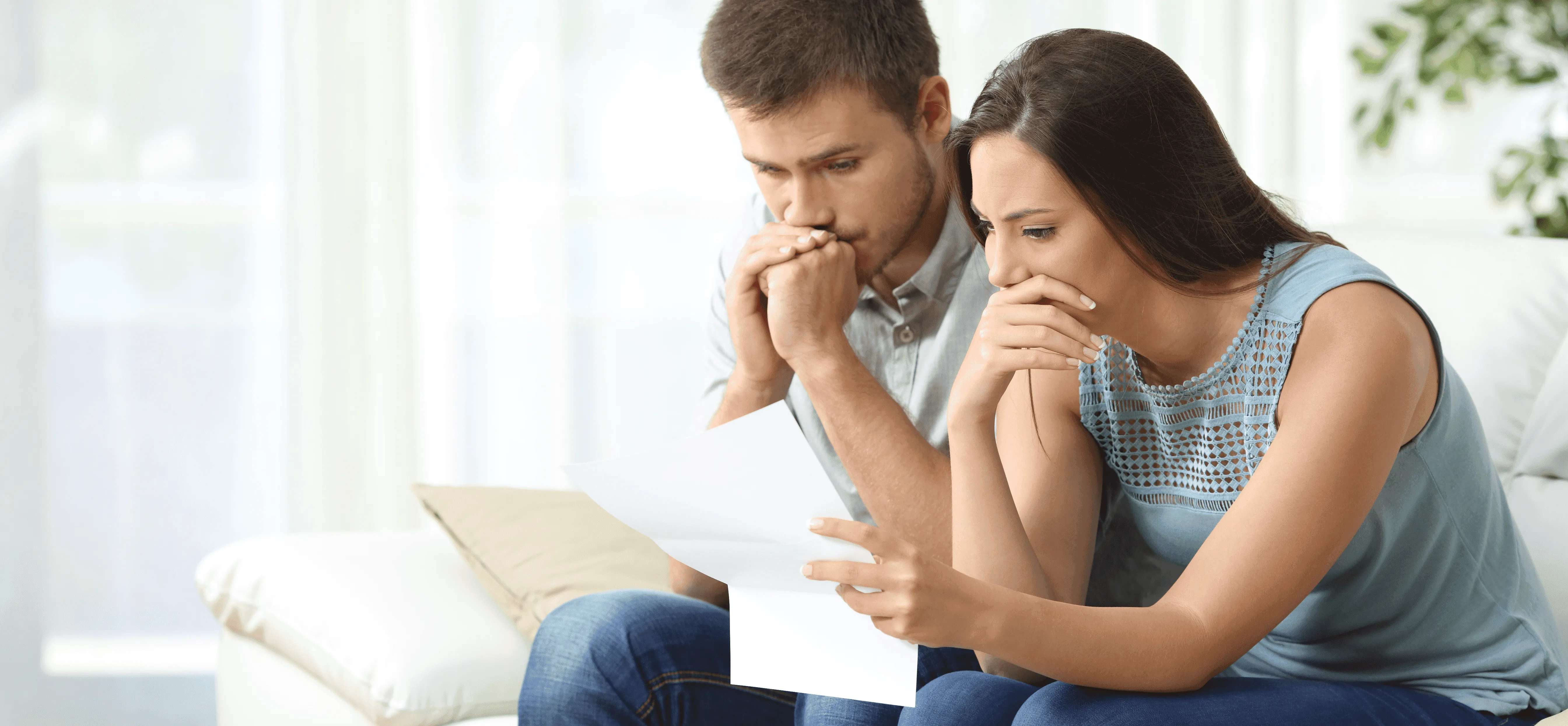 pareja sentada en el sofá y preocupada mirando un papel