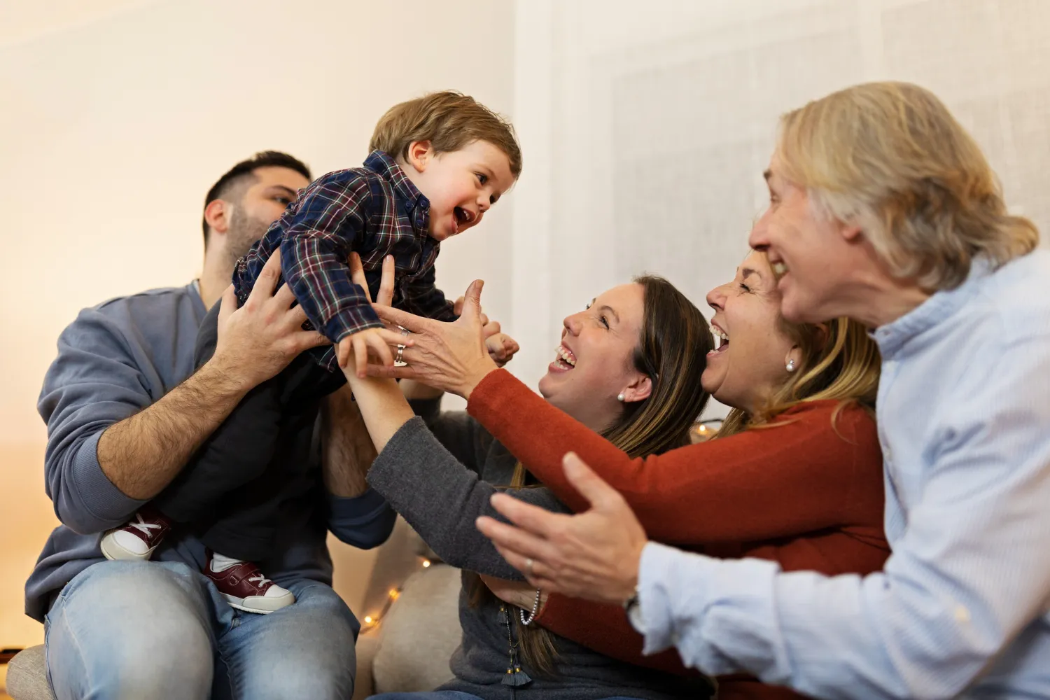 Familia riendo y jugando con un niño pequeño en un ambiente acogedor.