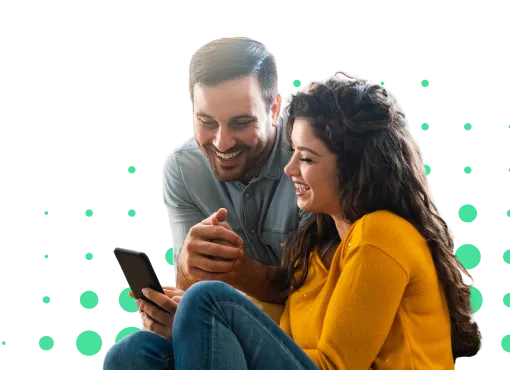 Pareja sonriente mirando un teléfono móvil, sentados en el suelo, con fondo negro y burbujas verdes.