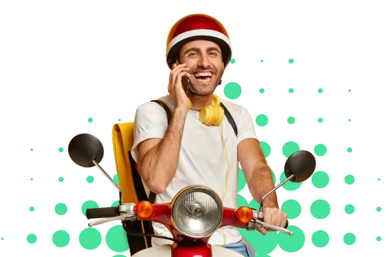 Hombre sonriente con casco rojo, hablando por teléfono mientras conduce una moto roja con detalles amarillos.