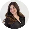 Mujer con cabello largo y castaño, sonriendo, vestida con camisa negra, fondo blanco.