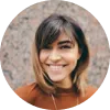 Mujer sonriente con cabello castaño claro y lacio, fondo de textura neutra.