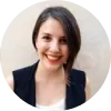 Mujer joven con cabello castaño y sonrisa, vestida con chaleco negro, fondo claro.