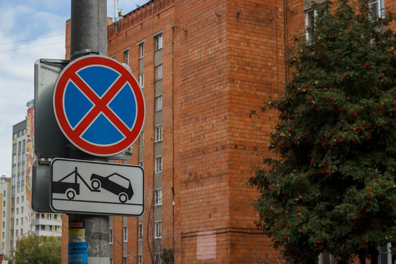 Señal de tráfico que indica prohibido aparcar, acompañada de un símbolo de remolque de vehículos. Fondo de edificio de ladrillo.