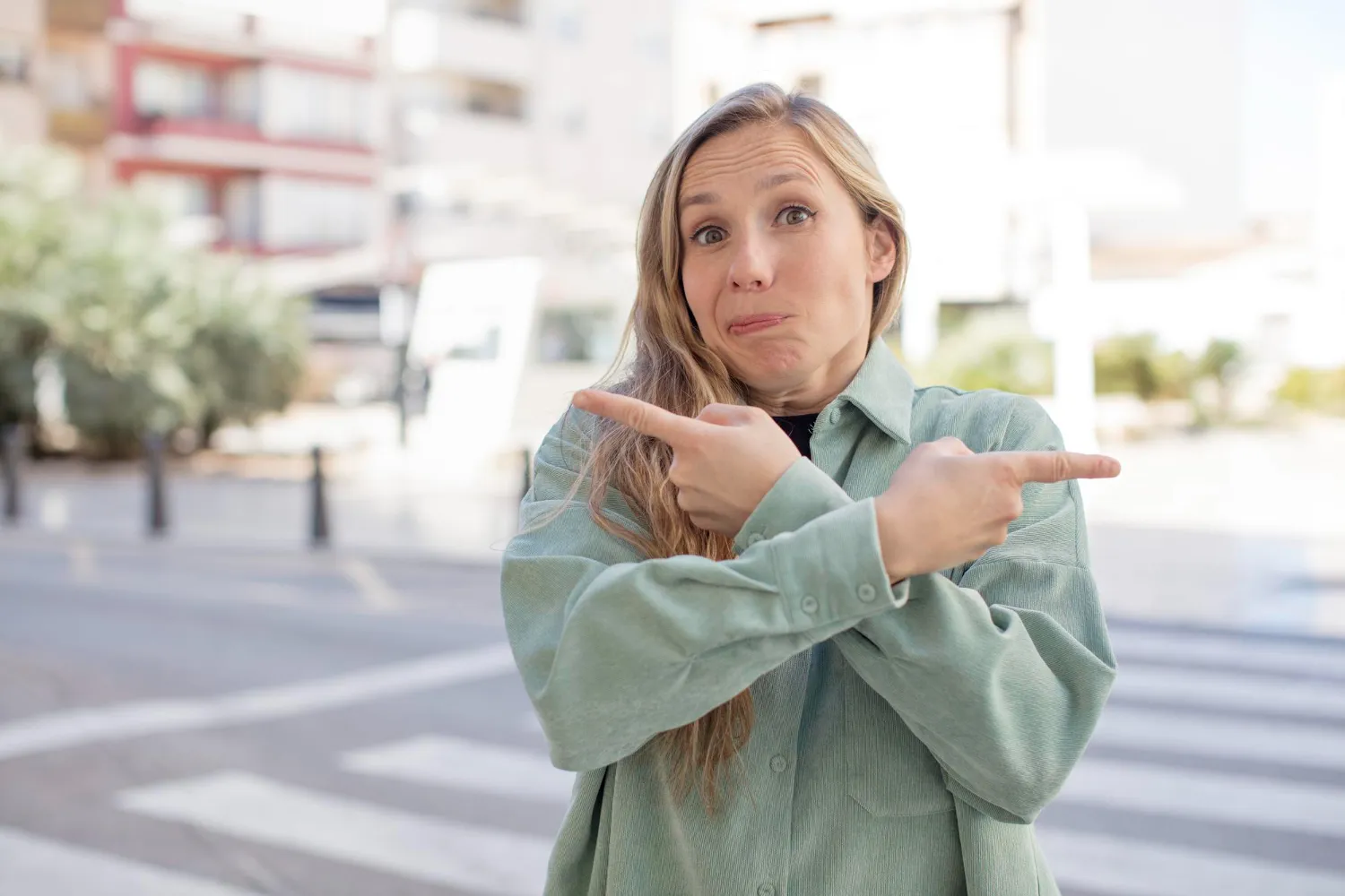 Mujer con camisa verde señalando hacia ambos lados, mostrando confusión o indecisión en un entorno urbano.