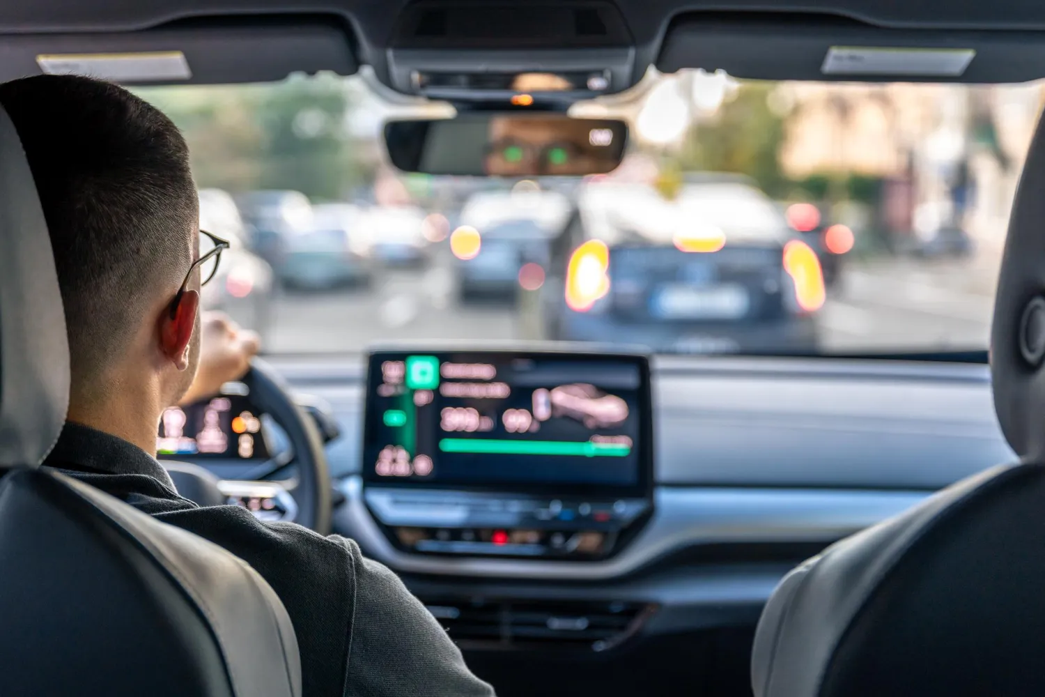 Conductor al volante de un coche moderno, mirando hacia el tráfico y la pantalla digital del tablero.