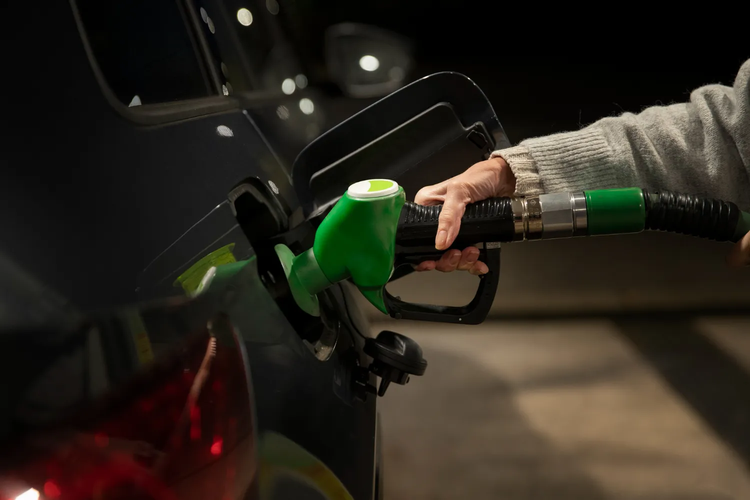 Mano sosteniendo una manguera de combustible verde mientras se llena el tanque de un coche en una gasolinera.