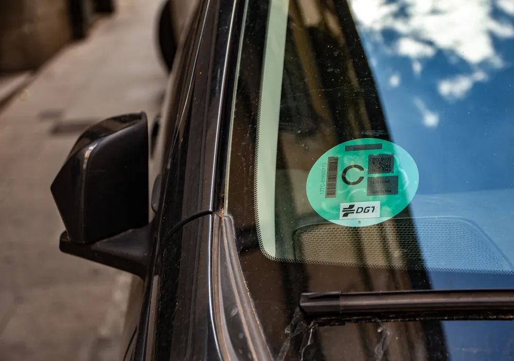 Etiqueta ambiental de color verde con letra "C" adherida al parabrisas de un coche negro.