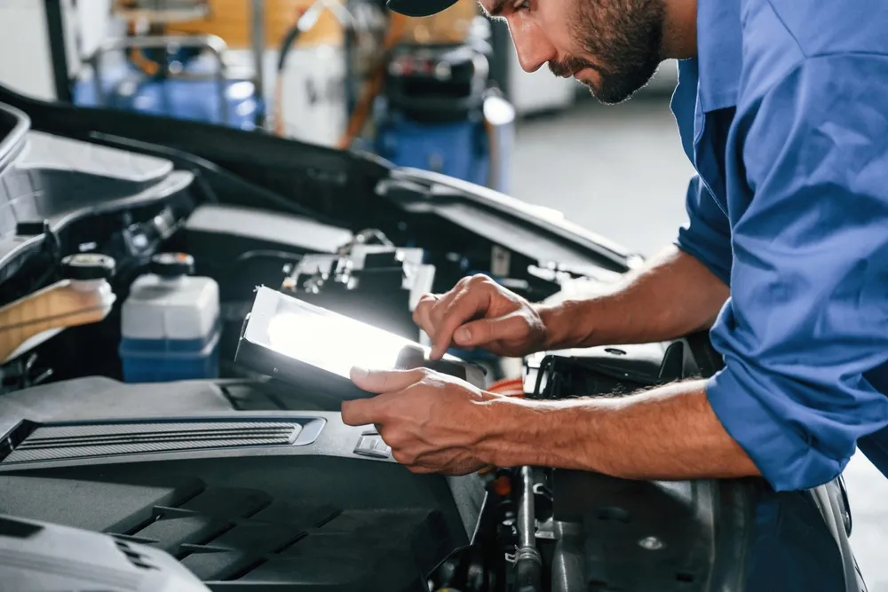 Mecánico revisando el motor de un coche mientras utiliza una tablet en un taller.