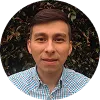 Hombre joven con camisa de cuadros, fondo de plantas verdes.