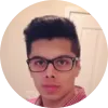 Joven con gafas y cabello oscuro, posando frente a una pared clara.