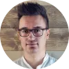 Hombre con gafas y cabello corto, sonriendo frente a un fondo de madera.