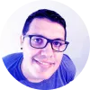 Hombre sonriente con gafas, cabello corto y oscuro, fondo claro.