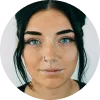Mujer con cabello oscuro y ojos azules, mirando directamente a la cámara, fondo blanco.