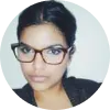 Mujer con gafas, cabello oscuro y piel clara, mirando a la cámara con expresión seria.