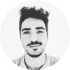 Retrato en blanco y negro de un hombre joven con cabello oscuro y barba ligera, sonriendo frente a un fondo claro.