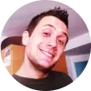 Hombre sonriente con cabello corto, fondo de habitación con muebles y pared clara.