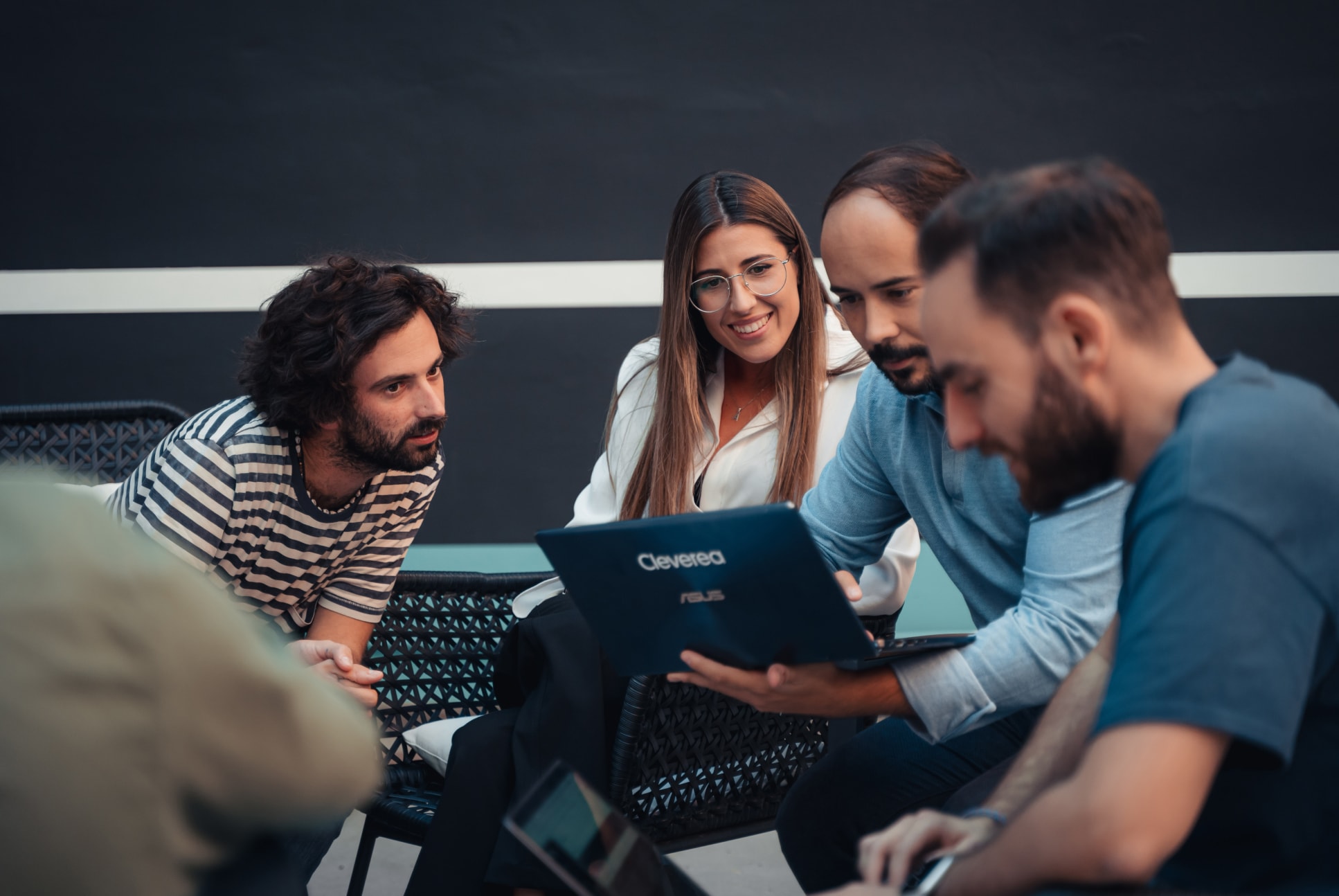 Miembros del equipo de Cleverea conversando y revisando una computadora portátil en un ambiente informal.