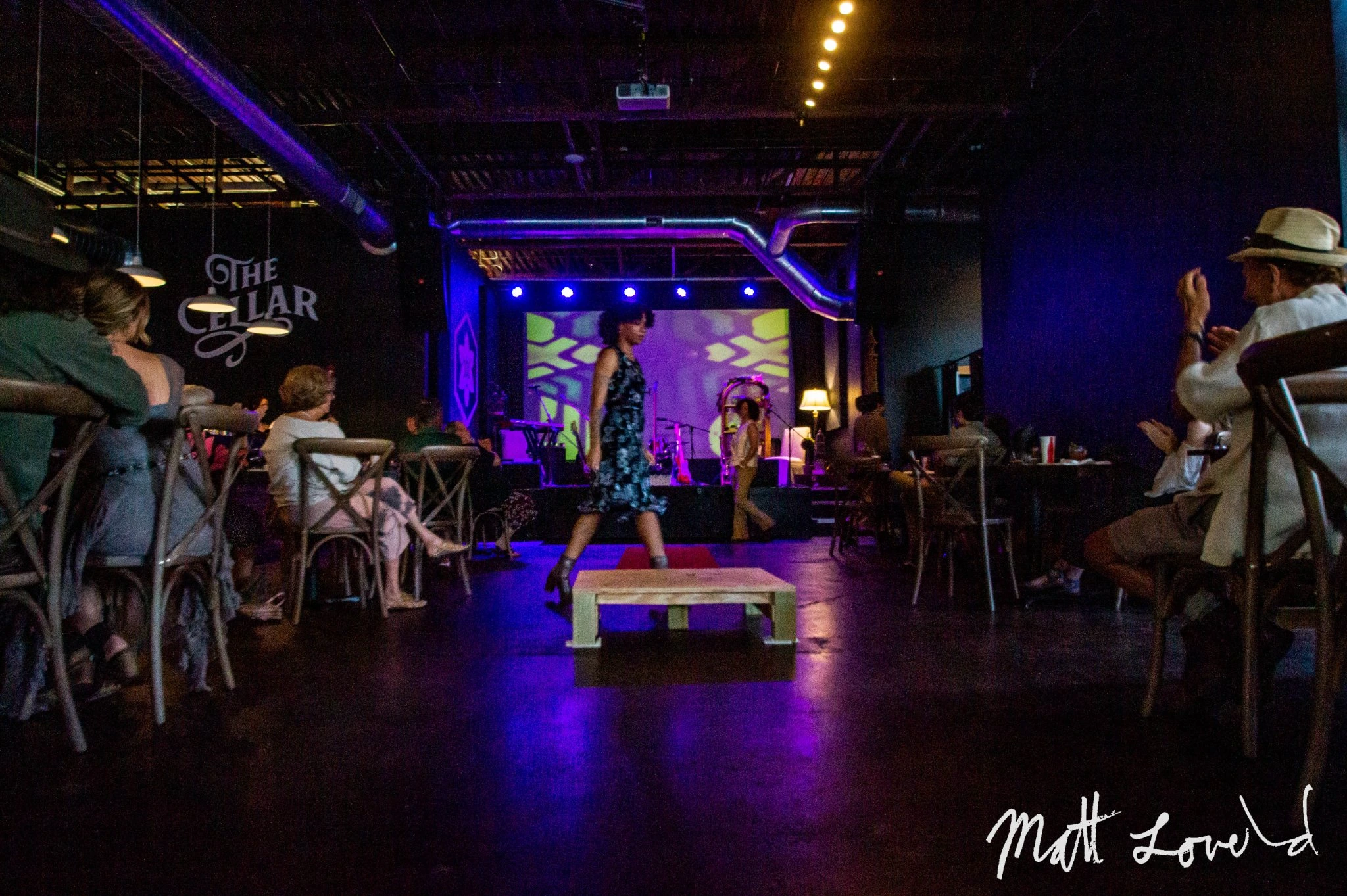 Runway photo with two models, showing some of the audience and a psychedelic pattern projected on the wall.